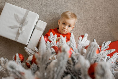 Top view of a cute little boy lying under the christmas tree next to wrapped chrismas presents