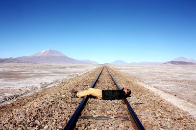 Man lying on railroad track against clear blue sky