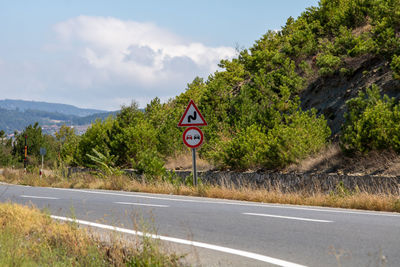 Road sign by trees against sky