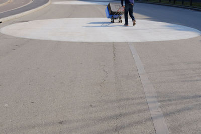 Low section of man pushing forklift with containers while walking on road