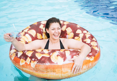 Happy young woman plus size body positive in inflatable doughnut circle swimming in the pool