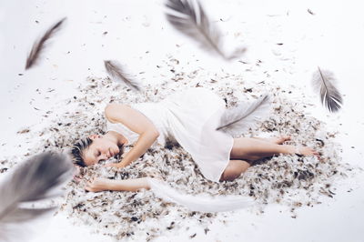 High angle view of woman lying on feathers over white background
