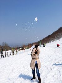 People playing on snow covered field against clear sky