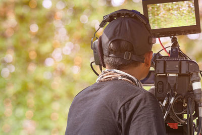 Rear view of man recording with camera against trees