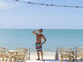 Man in swimwear and sunglasses posing in front of a tropical beach