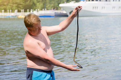 A man caught a poisonous snake while swimming in the water, holds it by the tail.