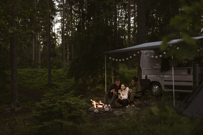 Friends camping in forest and sitting by campfire