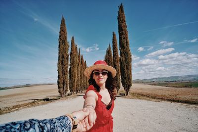 Portrait of woman holding cropped hand against trees