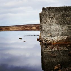 Reflection of wall on calm lake against sky