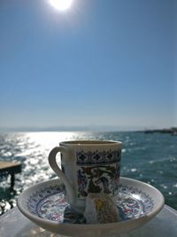 Close-up of coffee cup by sea against clear sky