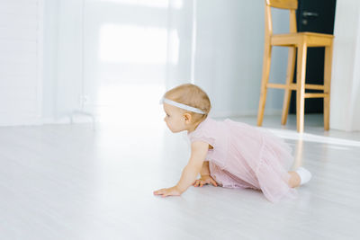 A one-year-old girl in a pink dress crawls on the floor in the children's room