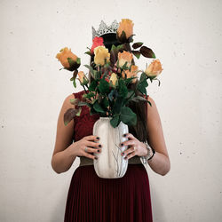 Woman holding flower vase while standing against wall