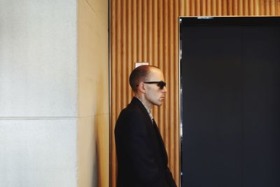 Side view of young man standing against wall