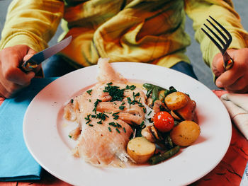 Midsection of man holding cutlery while sitting with food in plate at dining table