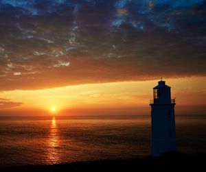 Lighthouse by sea against sky during sunset