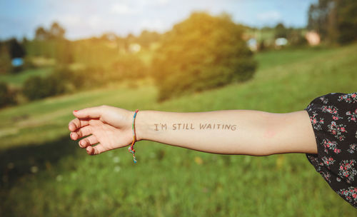 Cropped hand of woman showing text written on forearm at park