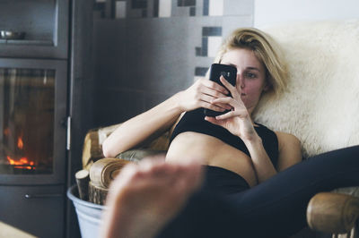 Woman using phone while sitting on armchair at home