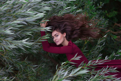 Portrait of young woman in maroon dress amidst shrubs