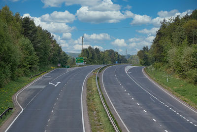 Empty road along trees and plants against sky