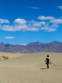 Rear view of backpack woman walking at desert against blue sky