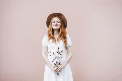 Portrait of young woman standing against white wall