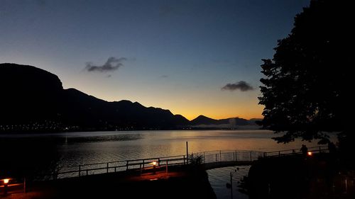 Scenic view of lake in front of silhouette mountains against sky