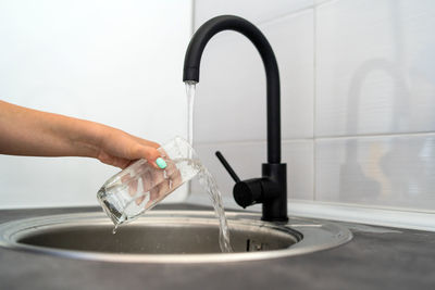 Cropped hand of woman pouring water in sink