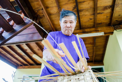 Low angle view of senior man making straw basket