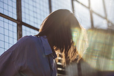 Close-up of young woman against glass window during sunny day