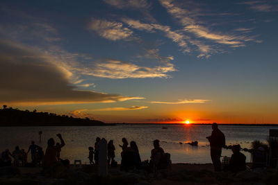 Silhouette people on beach against sky during sunset