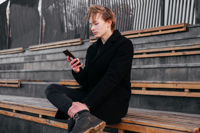 Young man using mobile phone while sitting on bench