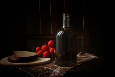 Close-up of fruits and bottle on table against black background