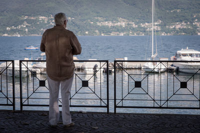 Rear view of man standing by railing against sea