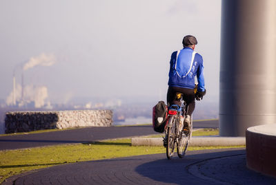 Rear view of man riding bicycle on road against sea