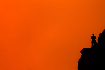 Silhouette people standing on rock against orange sky