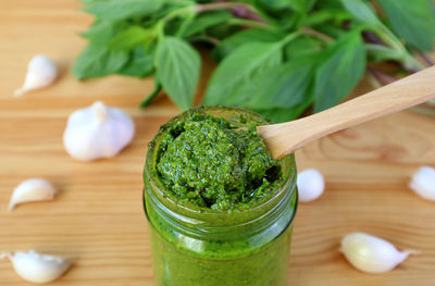 Closeup of homemade fresh basil pesto sauce on wooden table with its ingredients in background