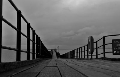 People walking on footbridge over sea against cloudy sky