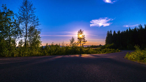 View of road by trees against sky during sunset