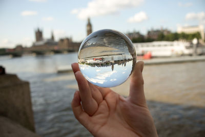 Close-up of hand holding crystal ball against river