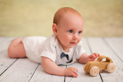 Cute baby boy lying by toy car on floor at home