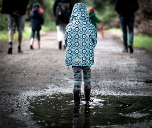 Rear view of boy walking in puddle on road