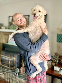 Portrait of man carrying dog while standing at home