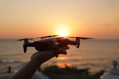 Cropped hand of woman holding drone at beach against sky