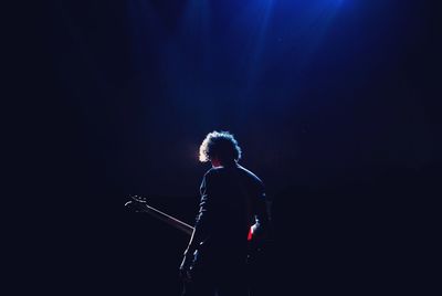 Rear view of man with guitar standing in darkroom