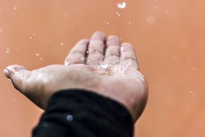 Close-up of water drops falling on hand against wall