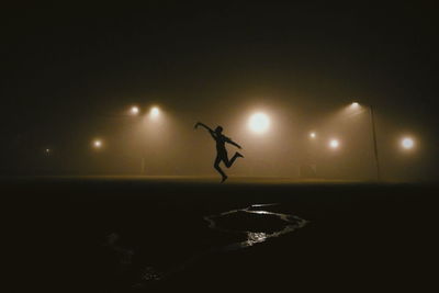 Silhouette man dancing against illuminated sky at night