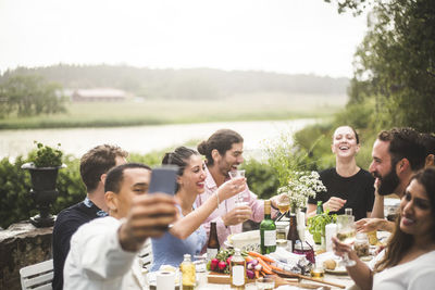 Man taking selfie of friends enjoying dinner at table during party in backyard