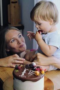 Portrait of blonde cute boy with mother eating cake at his birthday