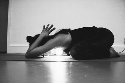 Side view of woman practicing yoga on mat at home