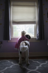 Girl with dog looking through window at home